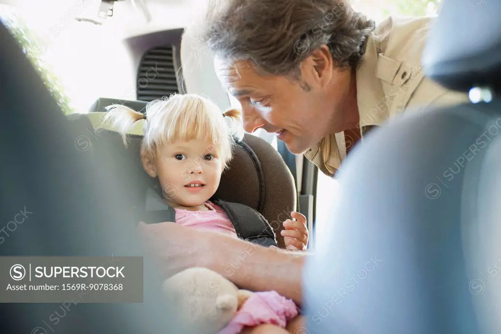 Father fastening little girl into car seat