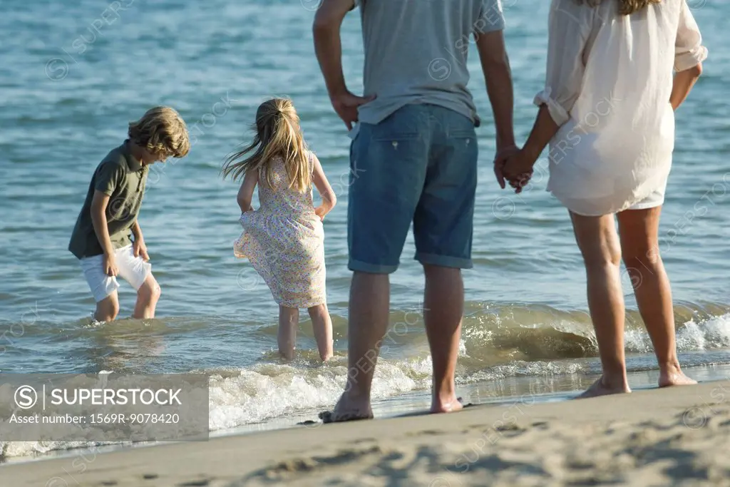 Family at the beach, parents watching as children play in surf