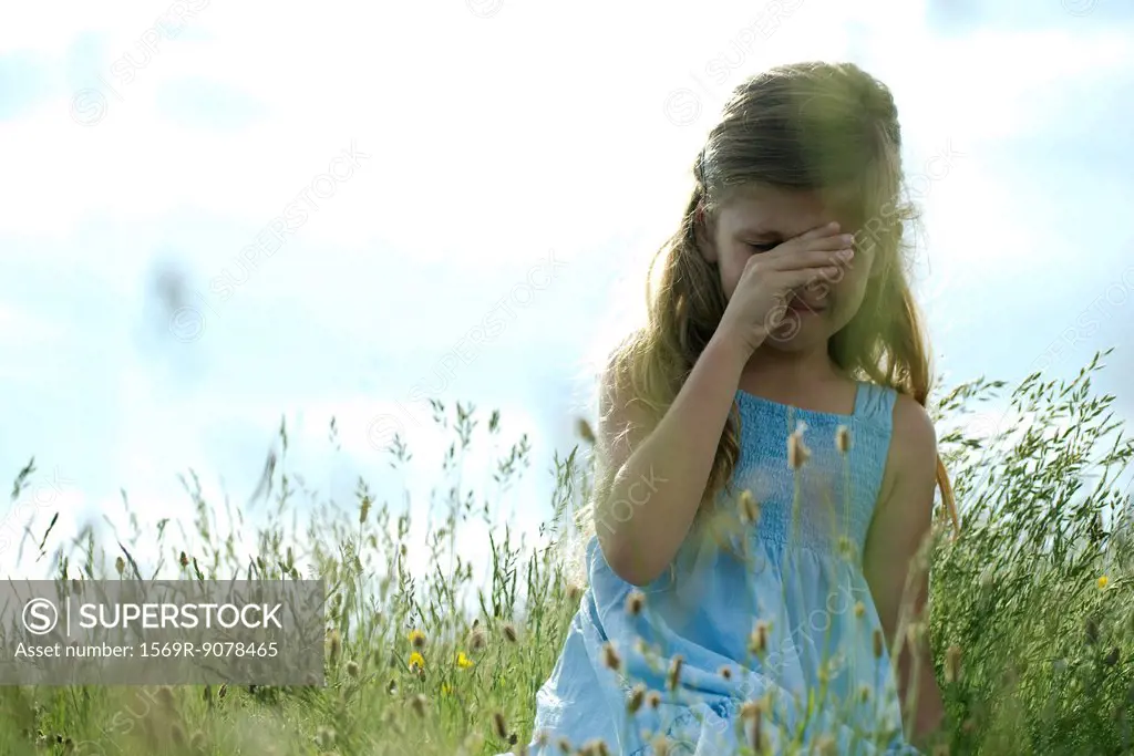 Girl crying in field, hand rubbing eyes