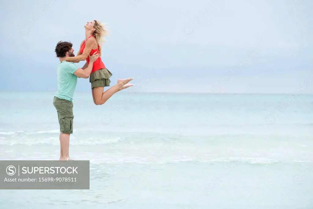 Couple at the beach, man lifting woman in air