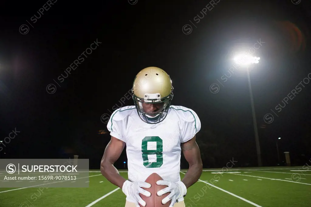 Football player holding ball, head down in concentration