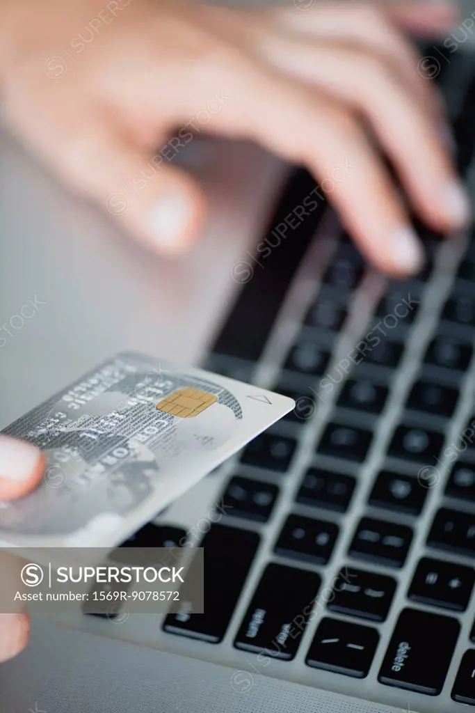 Woman holding credit card while using laptop computer, cropped