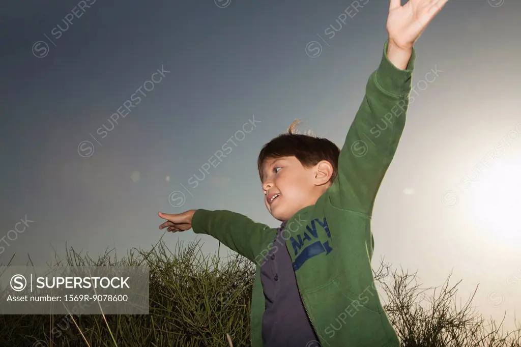 Boy playing outdoors with arms raised in air