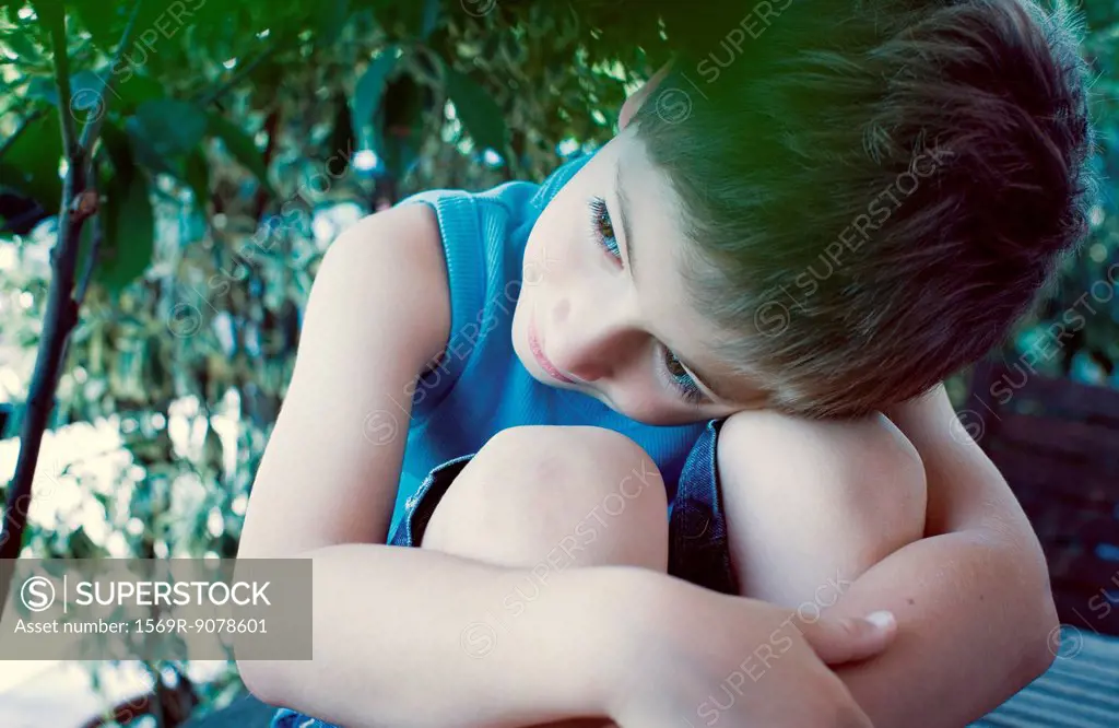 Boy resting head on knees, daydreaming