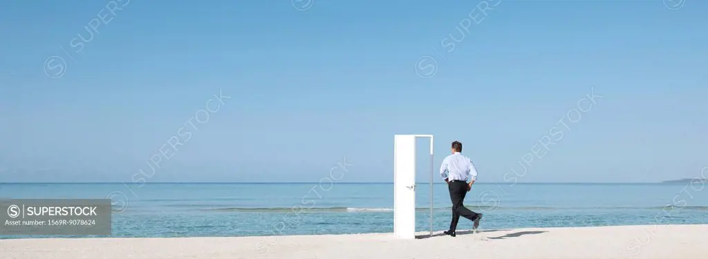 Man running on beach towards open door, rear view