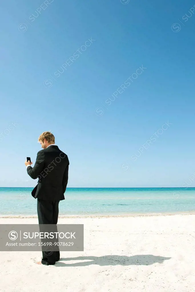 Young businessman using cell phone while standing on beach