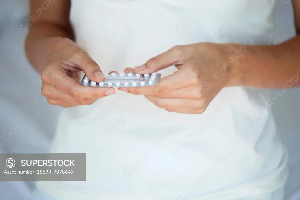 Woman holding birth control pills, mid section