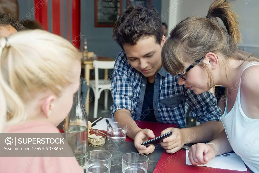 Friends hanging out together in cafe, looking at cell phone