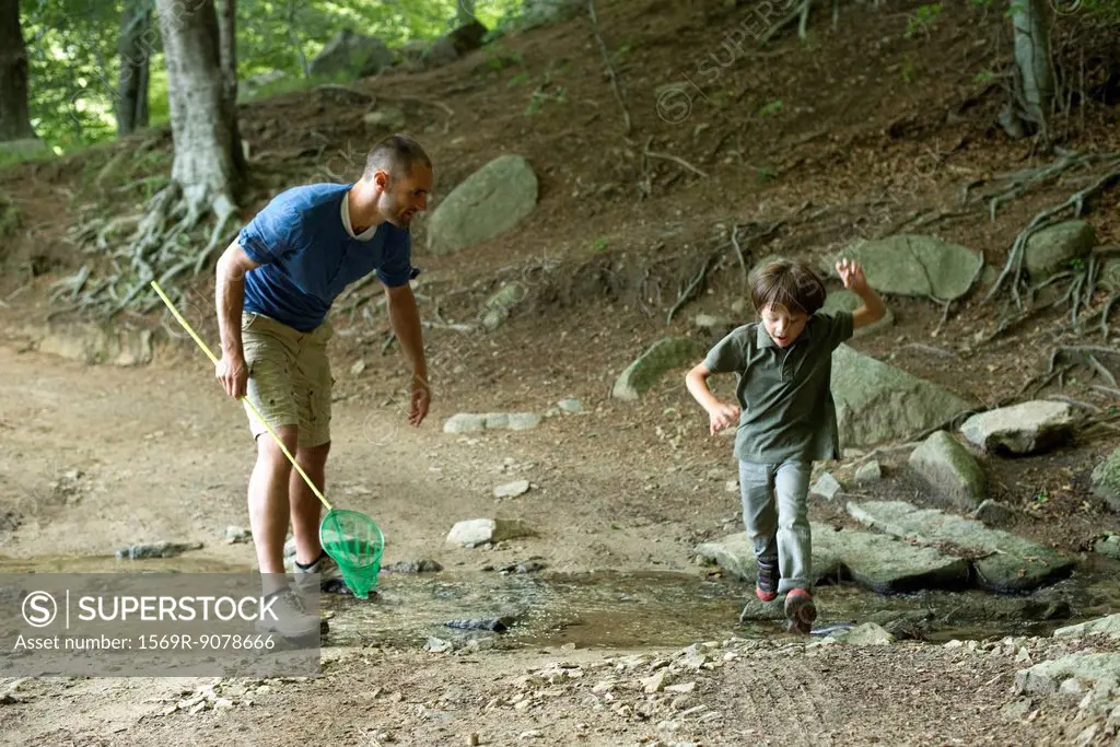 Father and son in woods, boy jumping over stream