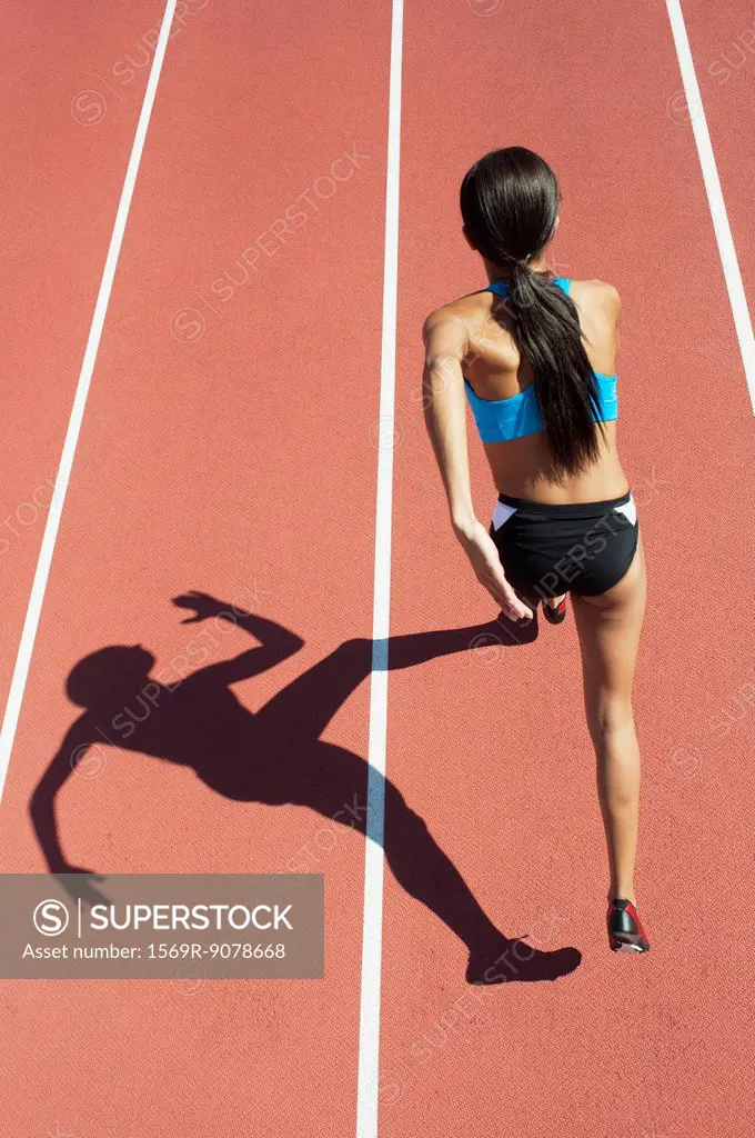 Female athlete running on track, focus on shadow