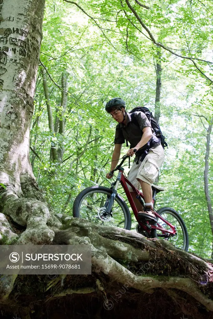 Young man riding bicycle in woods, low angle view