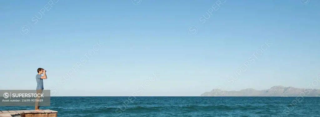 Man in distance standing on pier looking at ocean view through binoculars