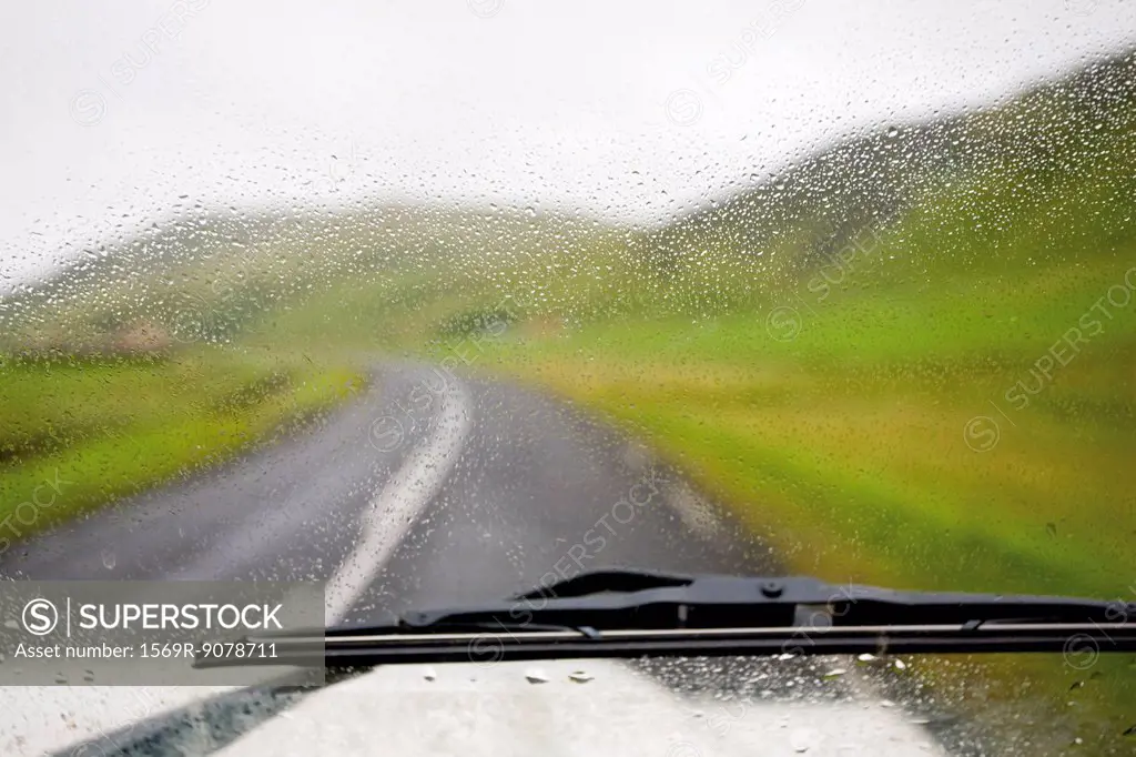 Road and countryside viewed through wet car windshield