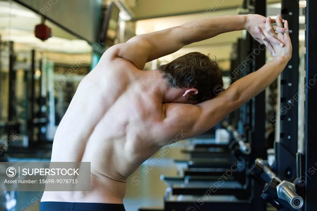 Barechested man stretching in weight room, rear view