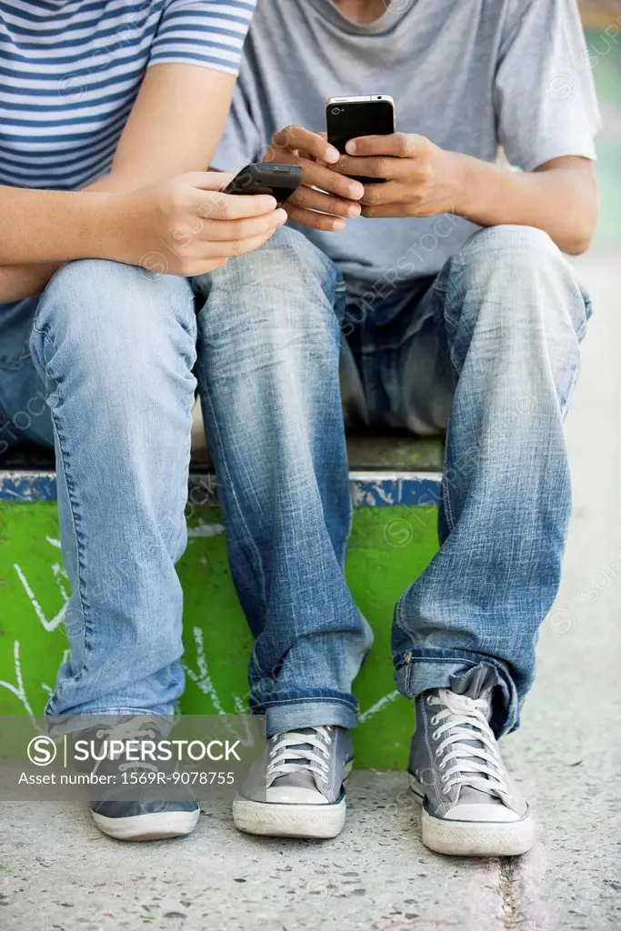Young men using cell phones, low section