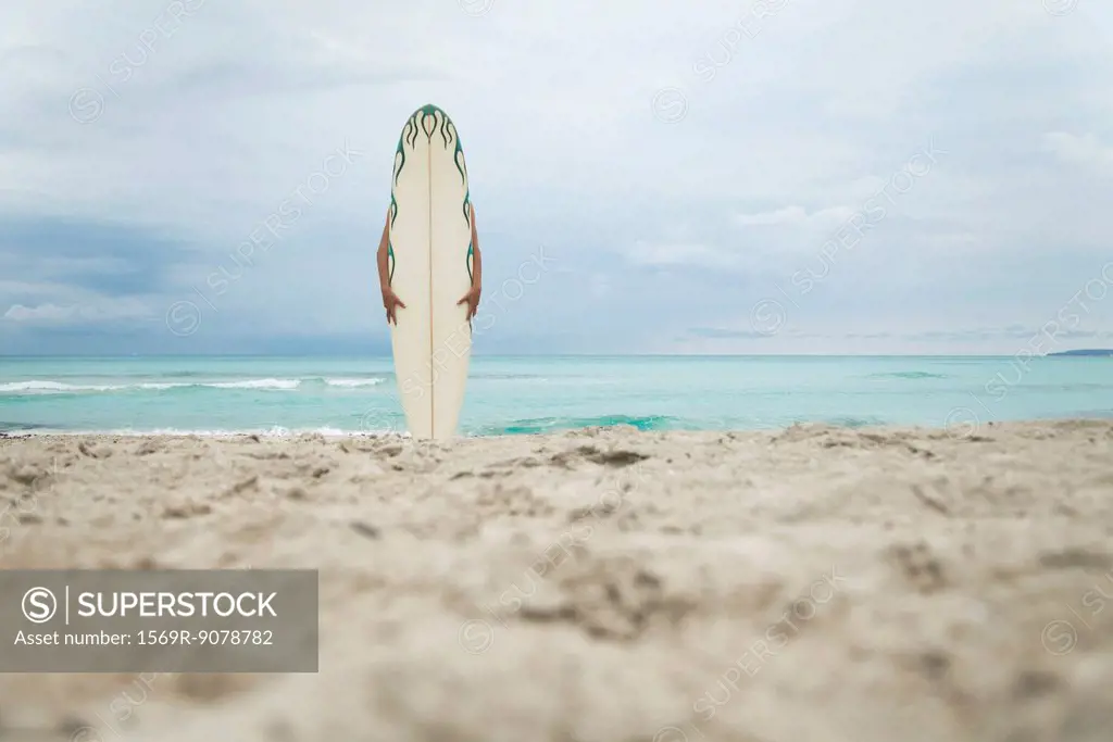 Person hiding behind surfboard at the beach