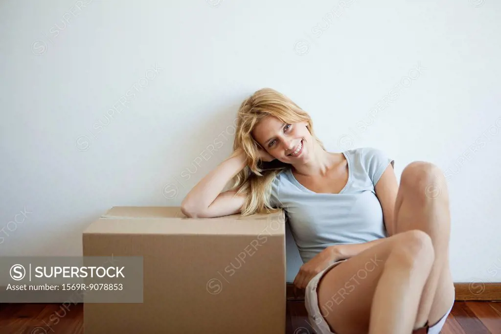 Young woman sitting on floor, leaning on cardboard box