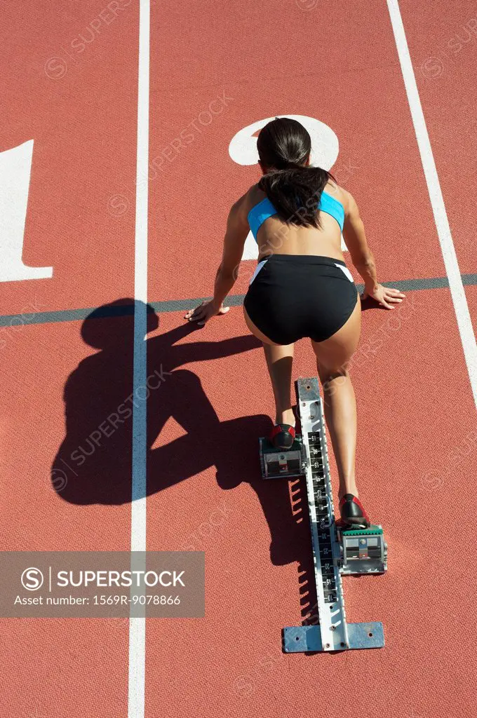 Female athlete in starting position on running track, rear view
