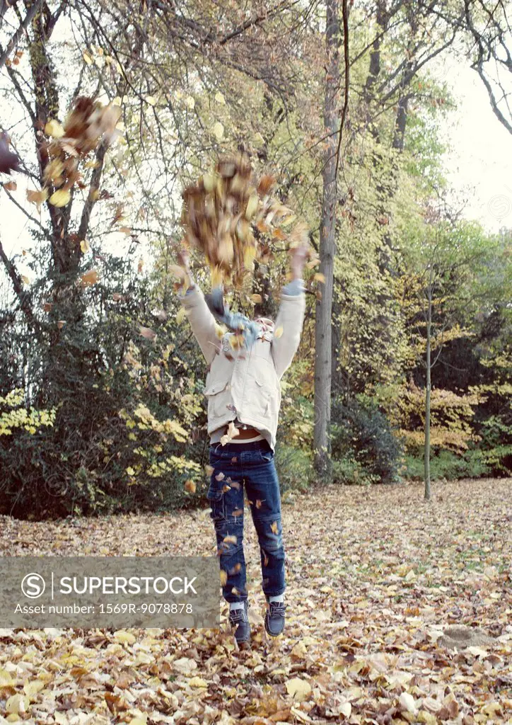 Boy jumping to reach tree branches with autumn leaves, blurred motion