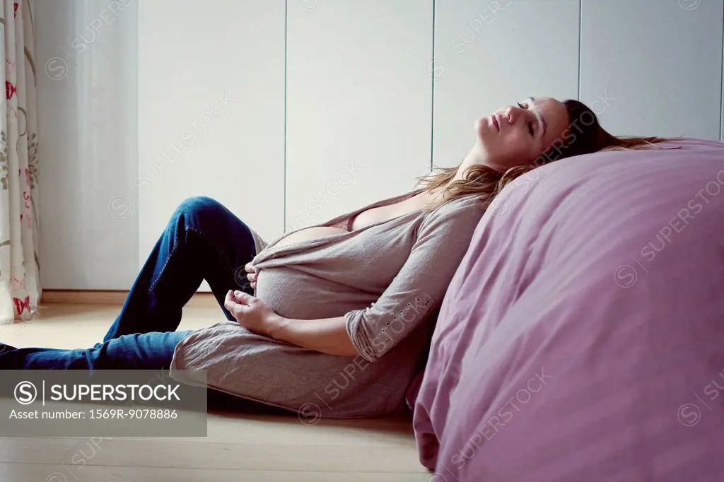 Pregnant woman leaning against bed resting