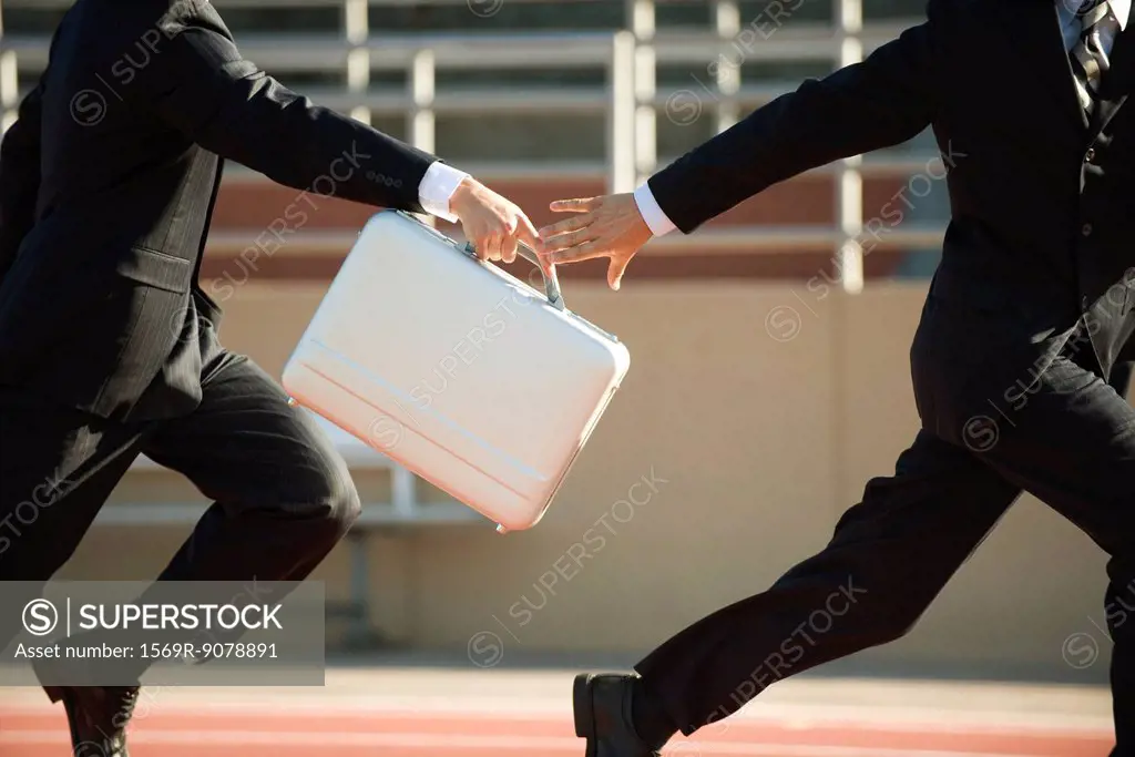 Businessmen running in relay race, handing off briefcase