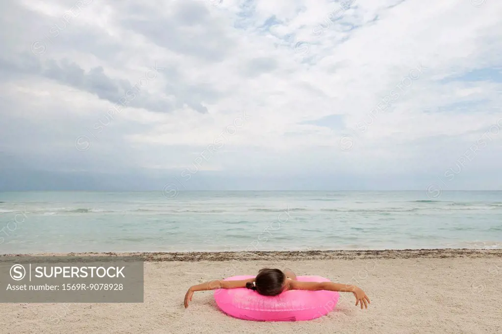 Girl lying on inflatable ring on beach, rear view