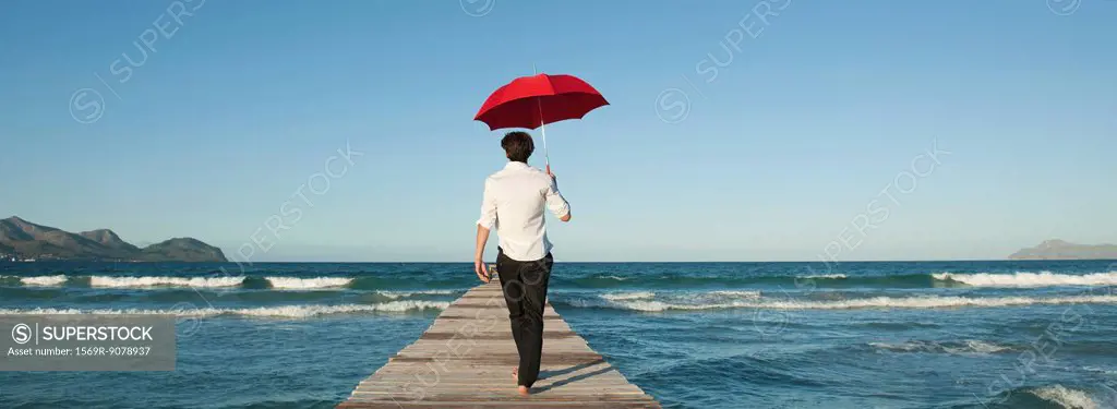 Man walking on pier with umbrella, rear view