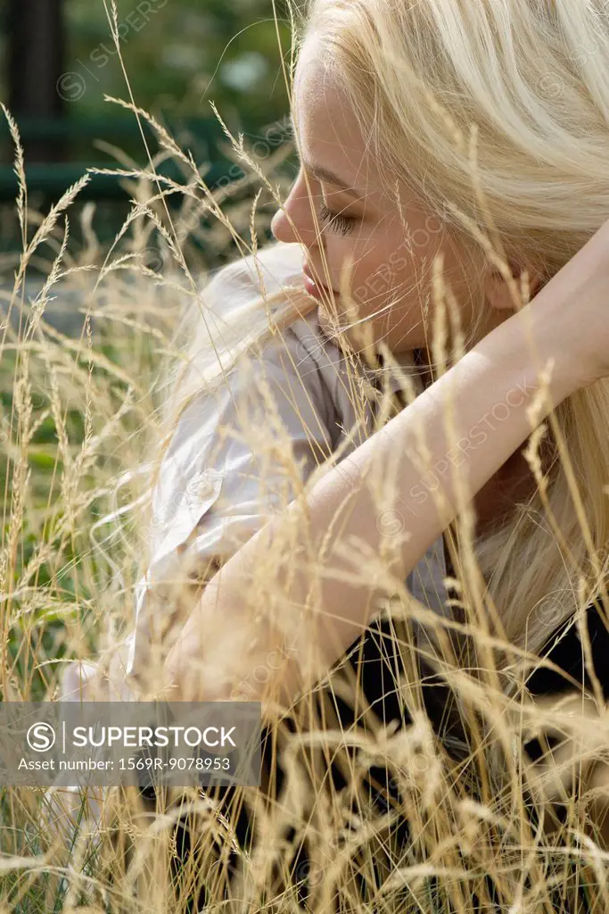Young woman sitting in tall grass with eyes closed