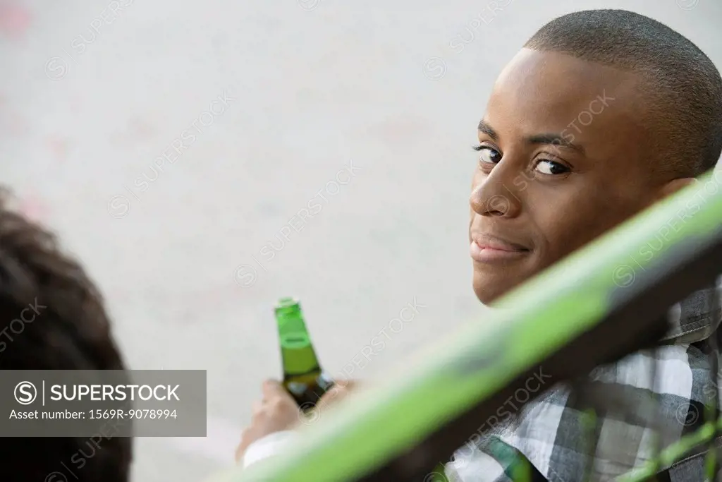 Young man holding beer bottle, looking over shoulder