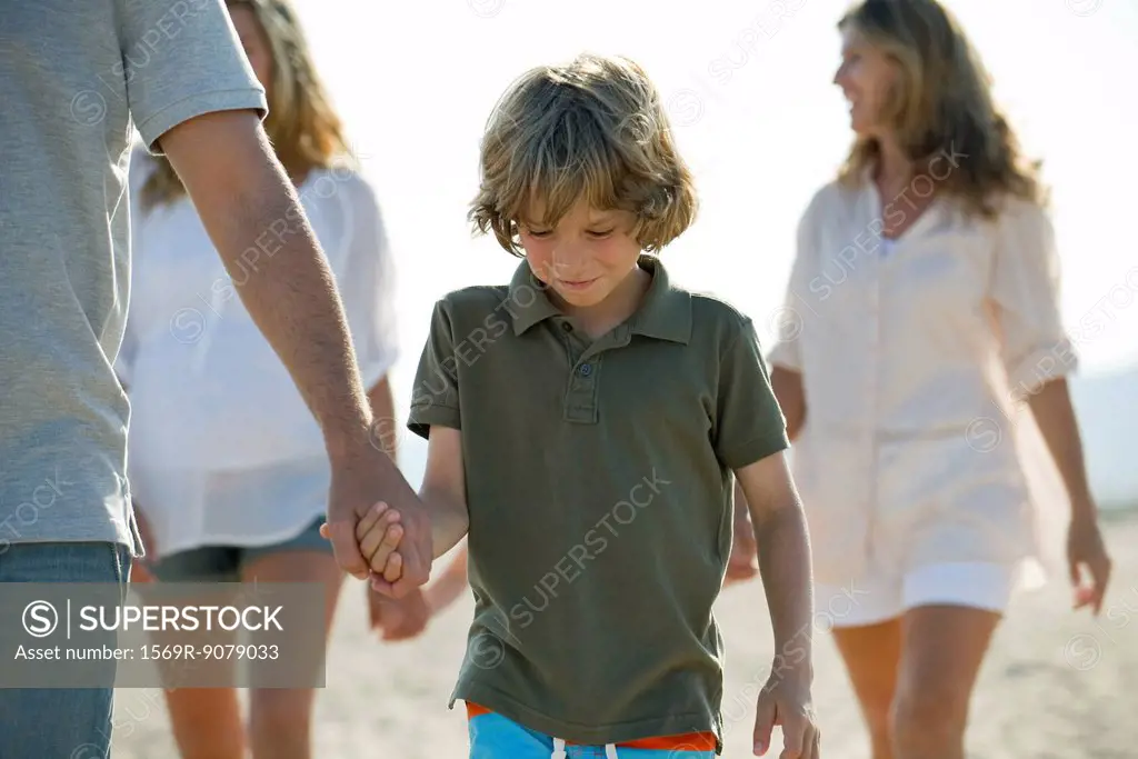 Boy walking on beach with family, holding father´s hand