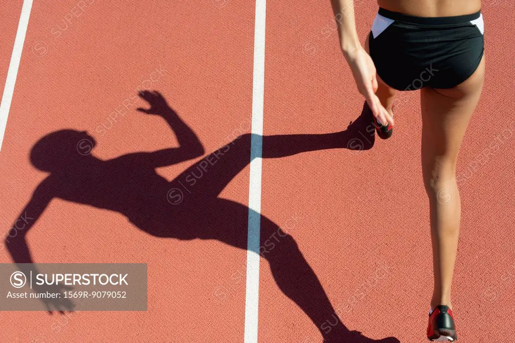 Female athlete running on track, low section, focus on shadow
