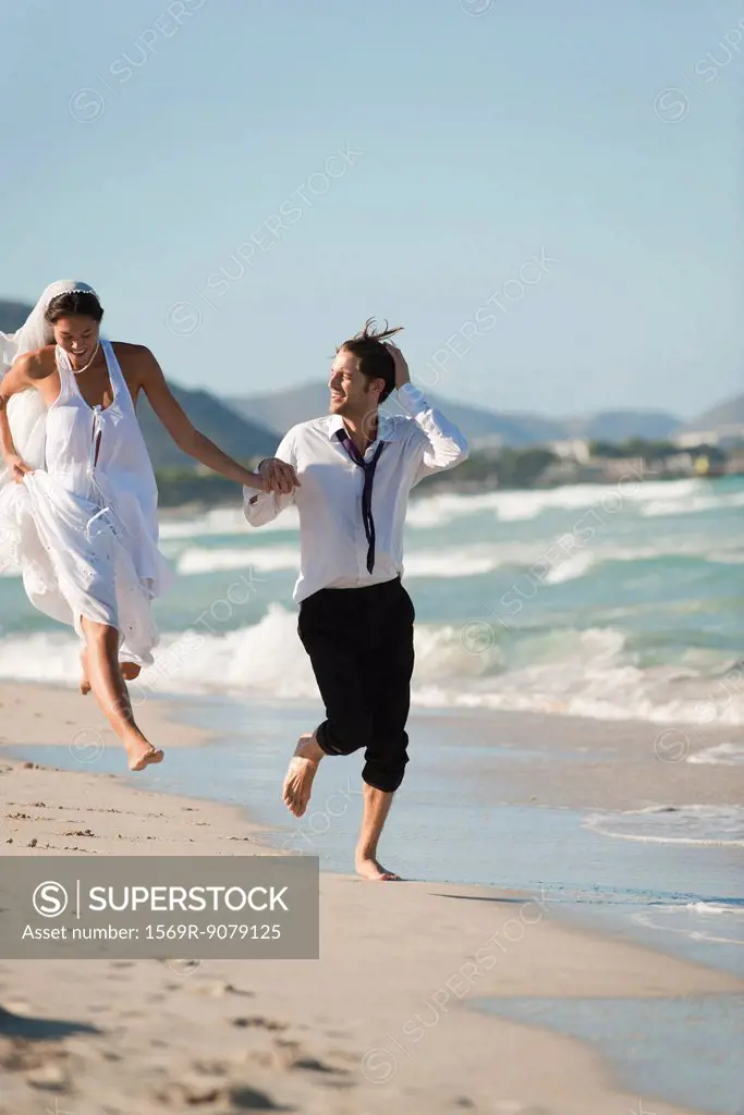 Bride and groom running hand and hand at the beach