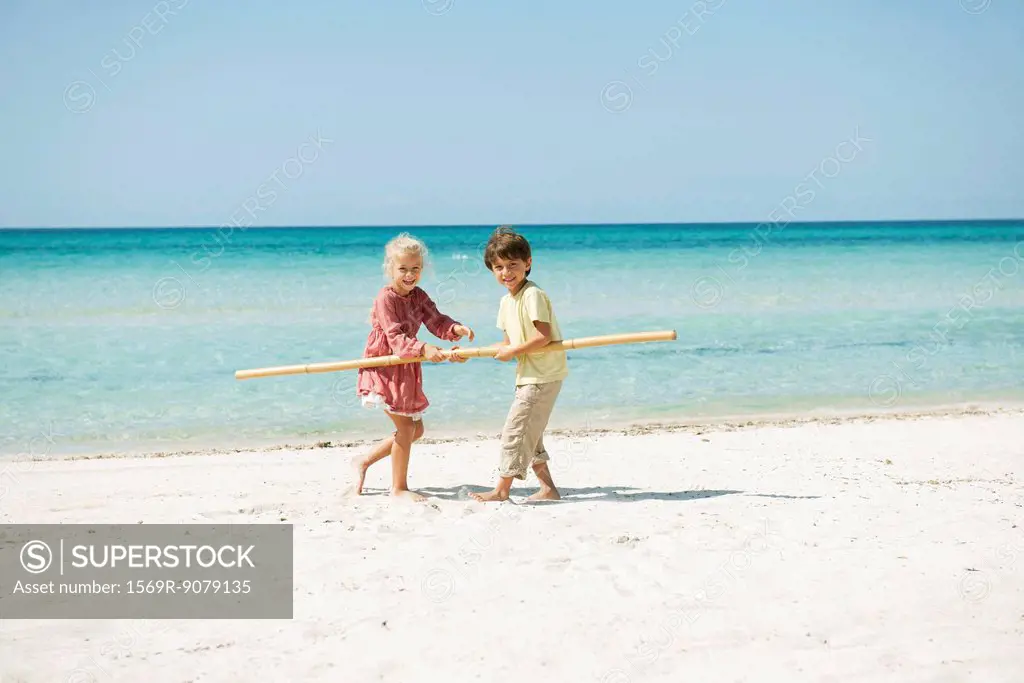 Boy and girl holding stick together on beach