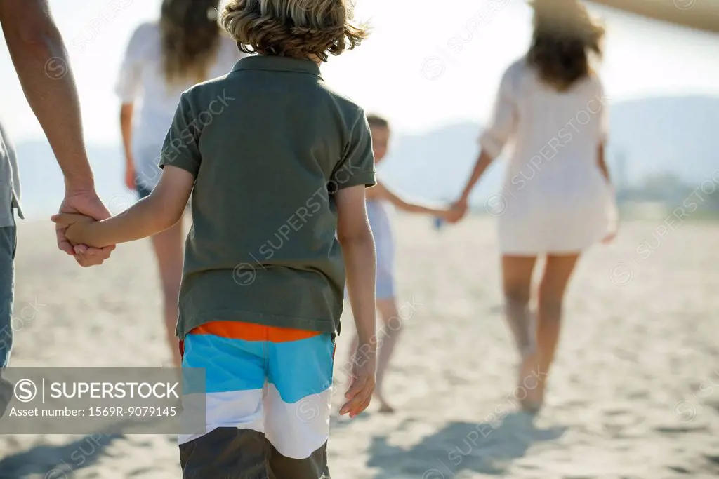 Boy at the beach with his family, holding father´s hand, rear view