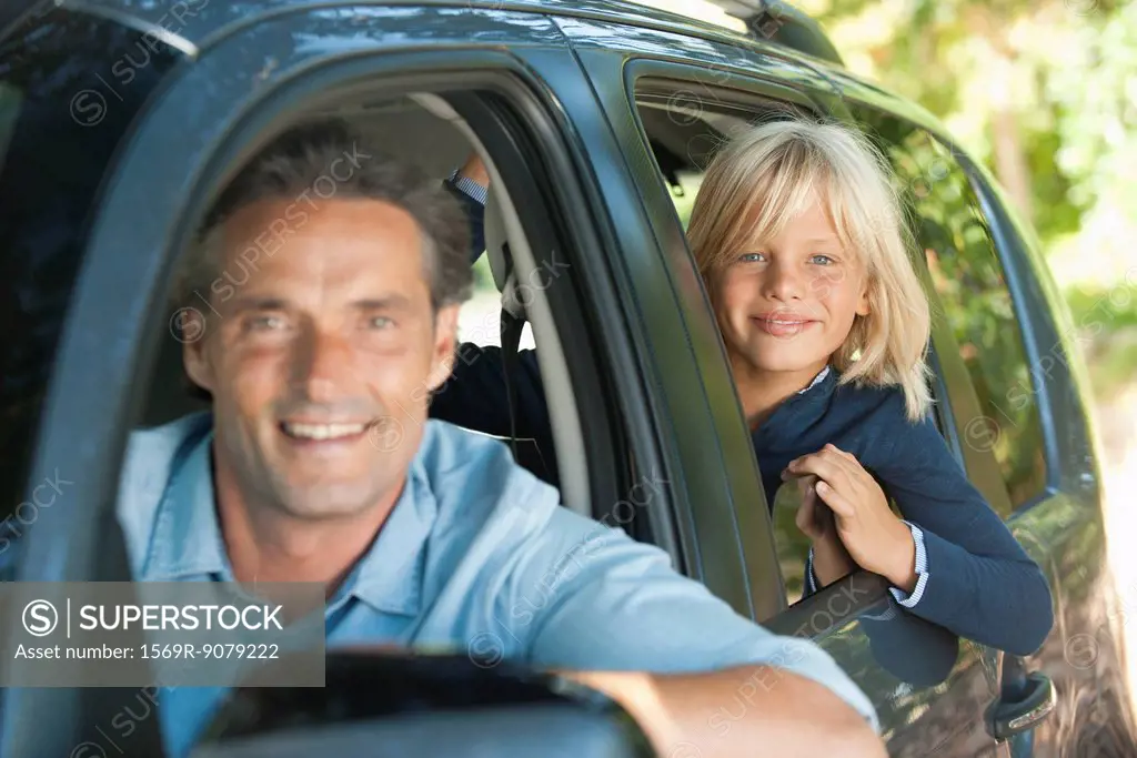 Boy riding in car with father, leaning out window and smiling at camera