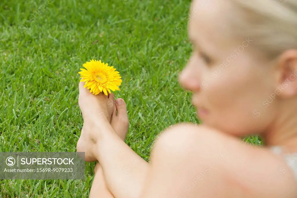 Woman holding flower between toes, looking away