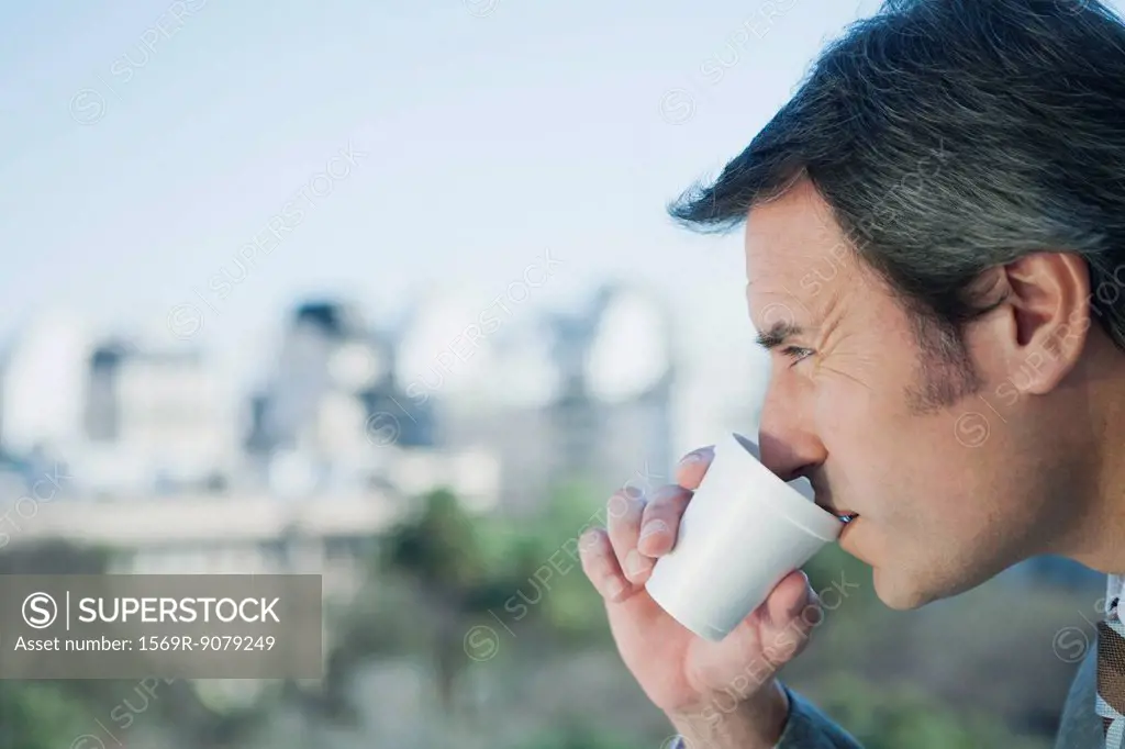 Mature businessman drinking from disposable cup, side view