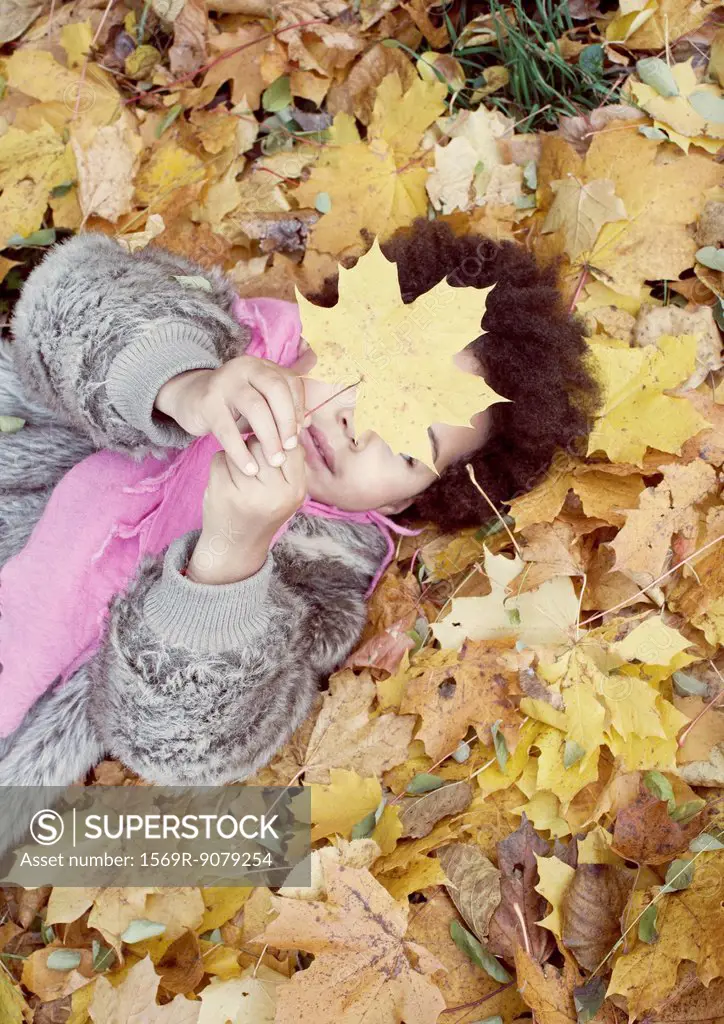 Little girl lying on bed of autumn leaves
