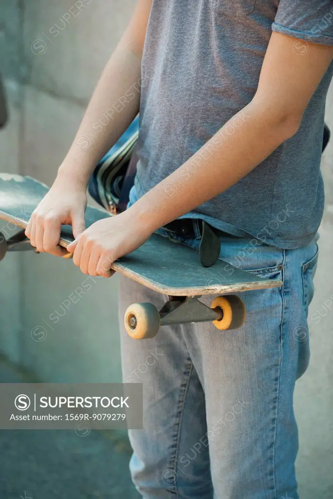 Man holding skateboard, mid section