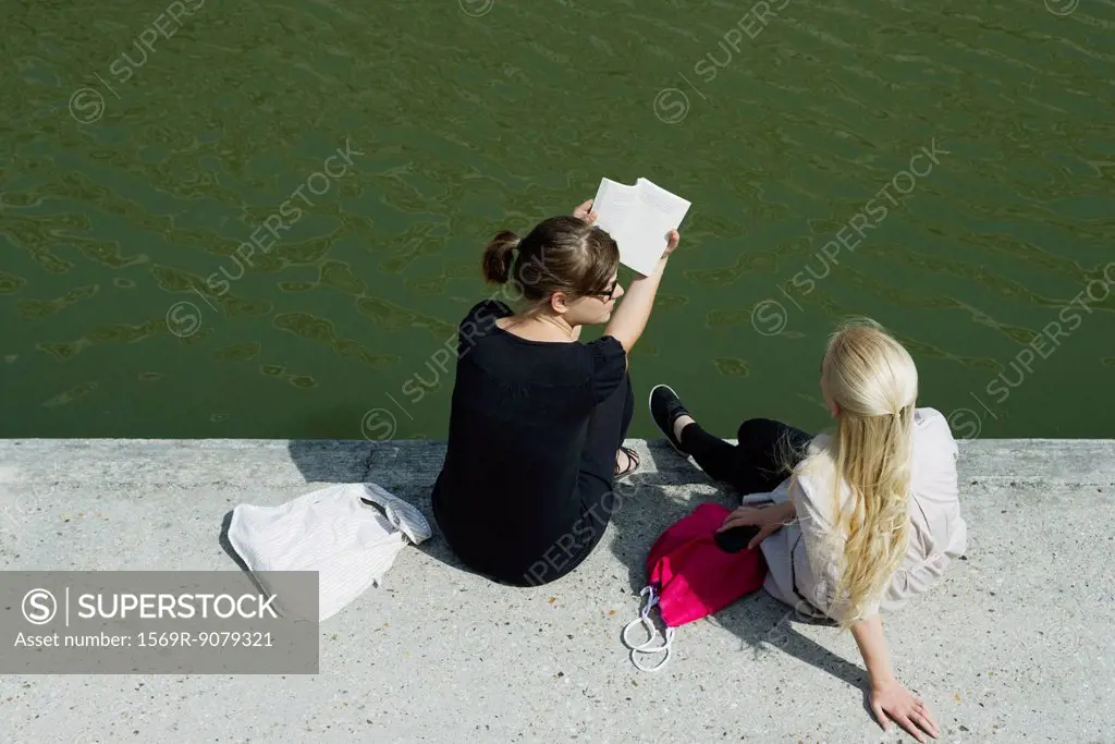 Young women relaxing together beside canal