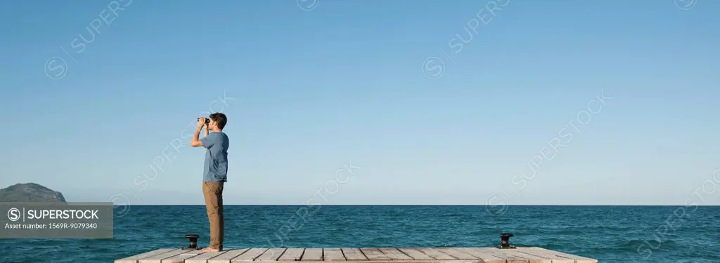 Man standing on pier looking at ocean view through binoculars, side view