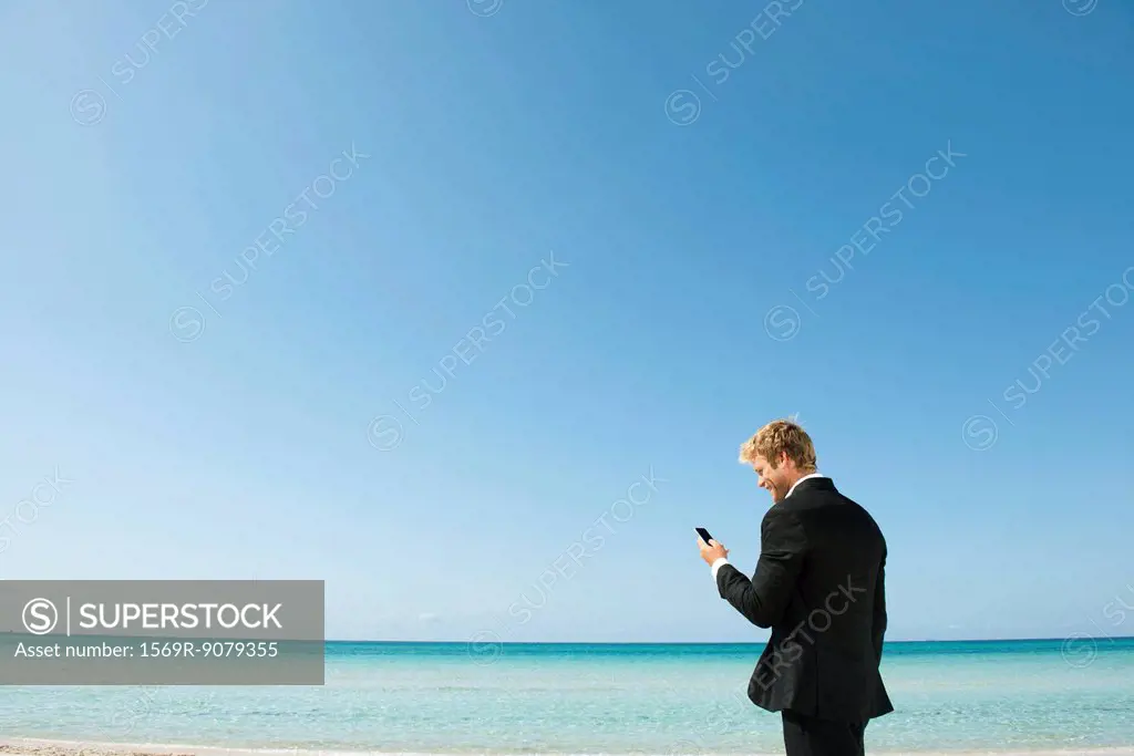 Young business man looking at cell phone by ocean
