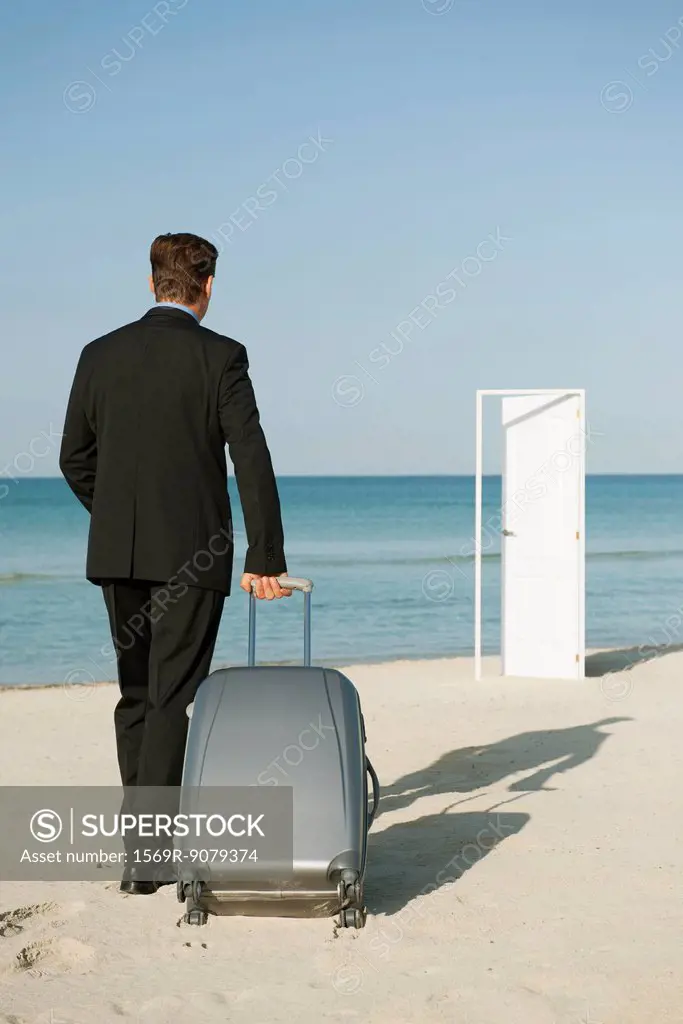 Businessman pulling suitcase on beach, half_open door in background