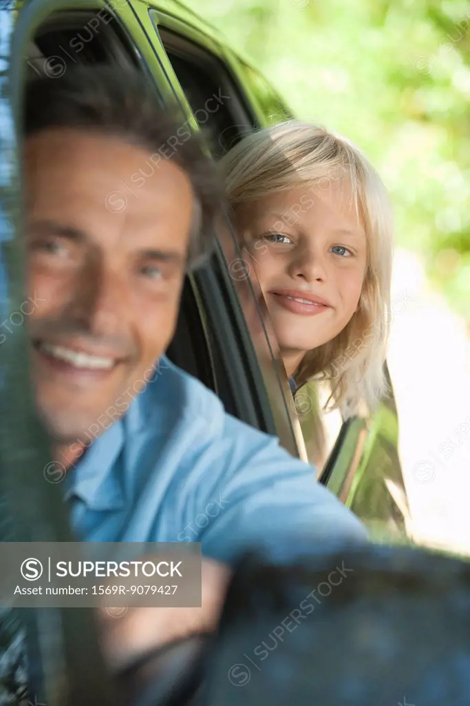 Boy riding in car with father, leaning out window and smiling at camera