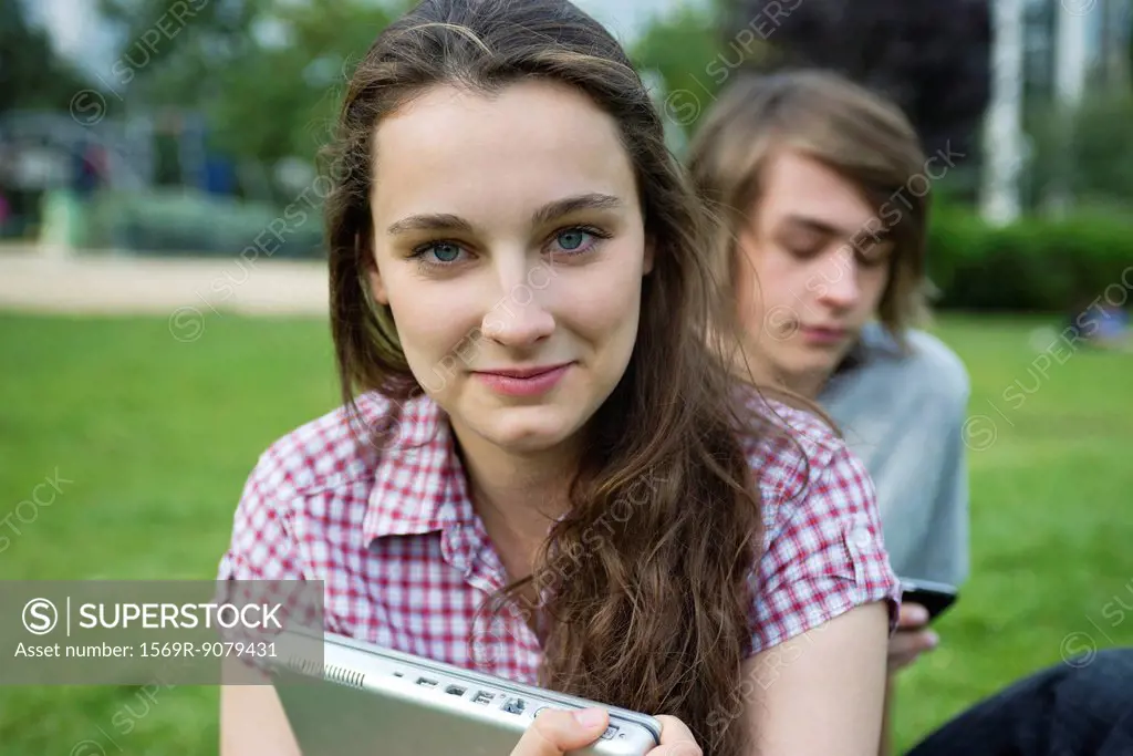 Young woman sitting outdoors, holding laptop computer, portrait
