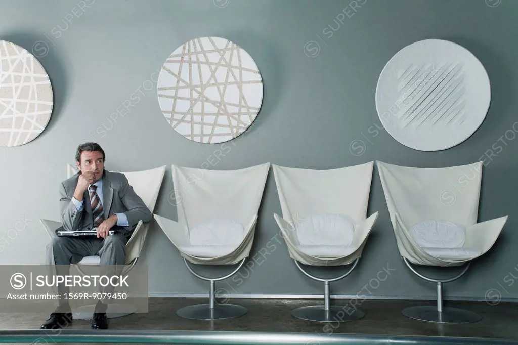 Mature businessman sitting at end of row of chairs in waiting room