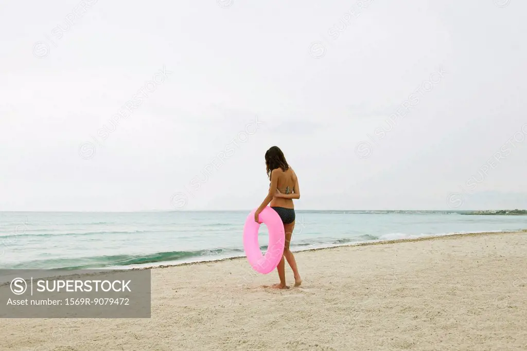 Woman standing on beach, holding inflatable ring, rear view
