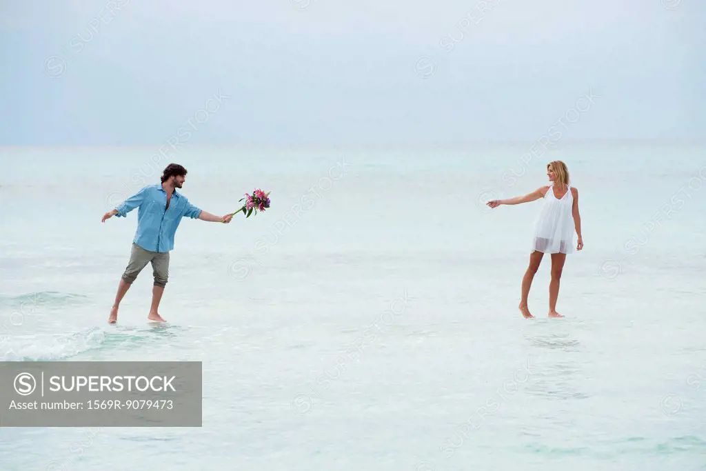 Couple walking on water towards each other, man holding out bouquet