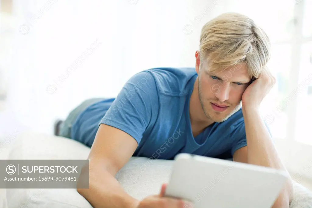Man lying on stomach looking at digital tablet