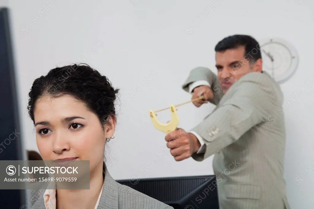 Businessman aiming slingshot at young female colleague
